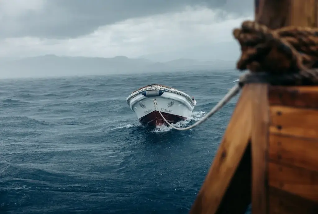 Red and white boat tied to the dock in wavy seas with mountains in the background.